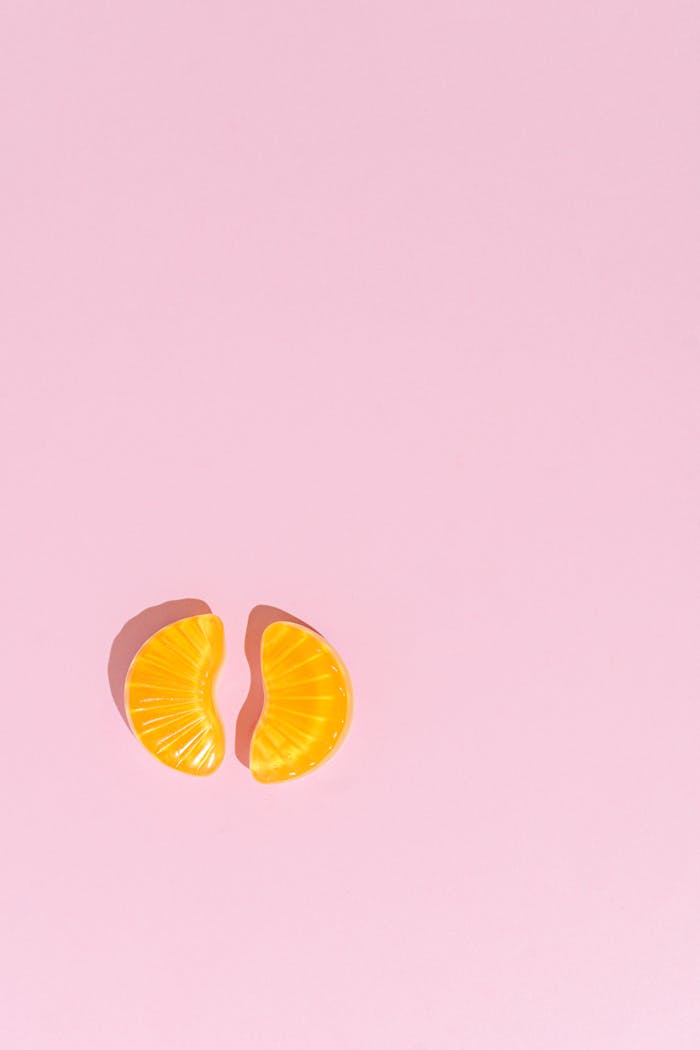 Minimalist photo of two orange jelly slices placed on a pastel pink background.